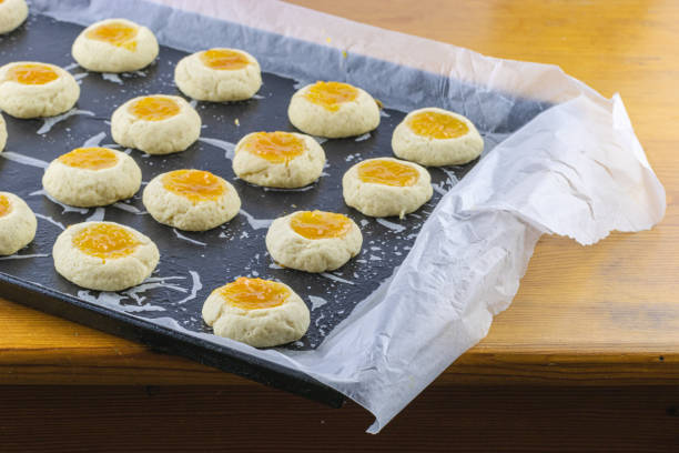 istock Half-cooked thumb print cookies filled with apricot jam on baking sheet. Selecive focus 1466353680