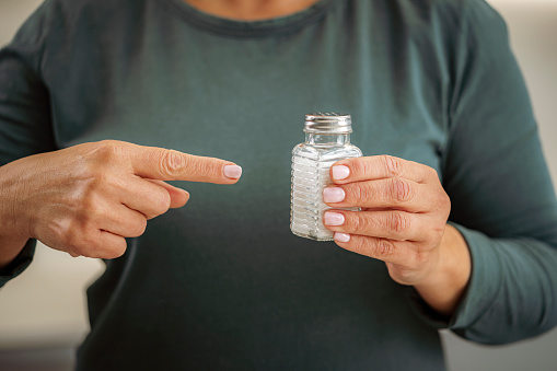 Healthy eating concept. Unrecognizable woman holding salt shaker and pointing with finger. High resolution 42Mp studio digital capture taken with Sony A7rII and Sony FE 90mm f2.8 macro G OSS lens