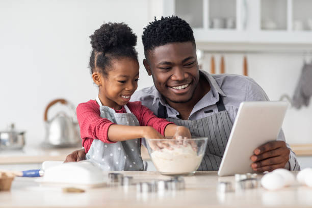 istock Adorable black father and daughter baking together, using digital tablet 1466358171