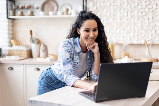 istock Remote business concept. Happy latin lady working with laptop in light kitchen interior, enjoying online job, copy space 1466358294