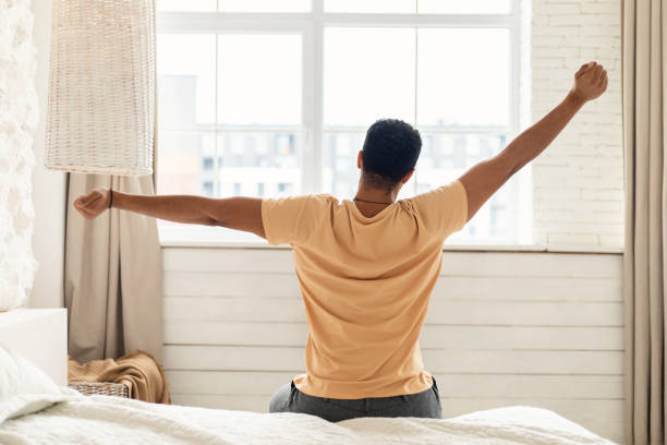 istock Man Sitting On Bed Stretching Arms In Bedroom, Back View 1466358389