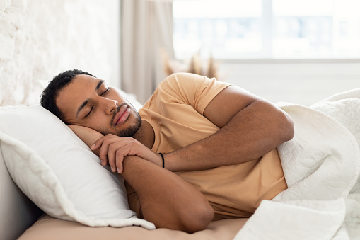 Sleeping Arabic Male Lying In Bed Holding Hands Near Face Resting Head On Pillow In Bedroom At Home. Asleep Man Napping Relaxing In The Morning. Healthy Rest And Recreation Concept