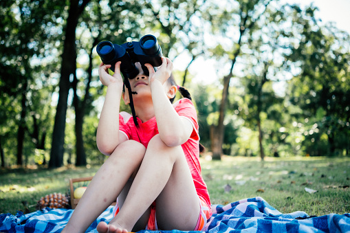 Asian children girl look through binoculars in public park