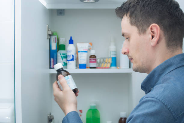 el hombre sostiene la instrucción de lectura de la botella de medicamentos o la prescripción en el envase. - armario de aseo personal fotografías e imágenes de stock