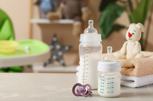 Feeding bottles with baby formula, pacifier and towels on light grey table indoors. Space for text