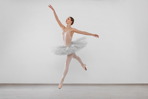A little girl ballerina is dancing on stage in a white tutu on pointe shoes a classic variation.