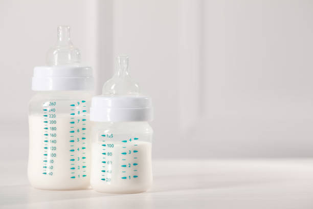 istock Feeding bottles with milk on white wooden table. Space for text 1466363109