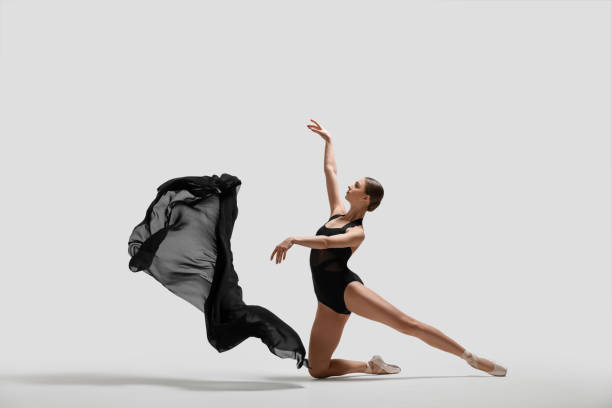 Graceful young ballerina practicing dance moves with black veil on white background