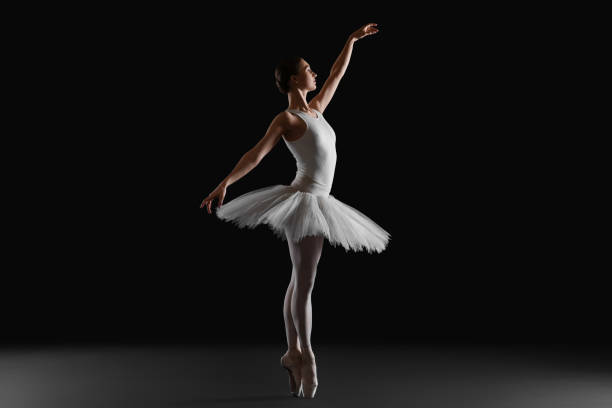 Young ballerina practicing dance moves on black background