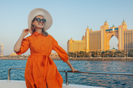 happy elegant woman in orange dress on yacht with Atlantis hotel in background. Dubai, United Arab Emirates