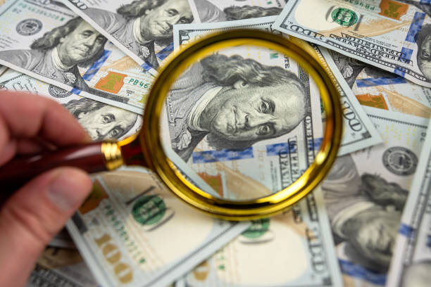 istock a man's hand holds a magnifying glass and looks at a dollar bills 1466365468