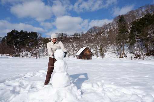 Asian man making a snowman in Shrirakawa-go, Gifu, Japan