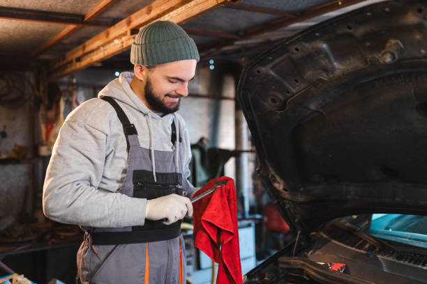 porträt eines jungen mechanikers, der einen steckschlüssel vor einem auto mit offener motorhaube in seiner garage hält - waistup stock-fotos und bilder