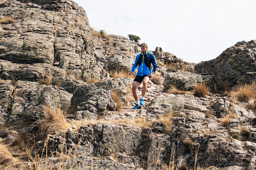 Young man practising trail running in the high mountains, while descending down the mountainside