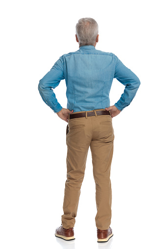 old man with grey hair in his 60s holding hands and posing from back view on white background while standing in studio