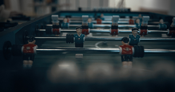 Plastic miniature foosball players figures spinning on table close up. Unrecognized energetic boys hands pulling rods. Children trying score goal playing match together. Teenagers entertainment.