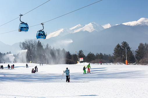Bansko, Bulgaria - February 11, 2023: Bulgarian winter ski resort panorama with gondola lift cabins, Pirin mountain peaks view and slope