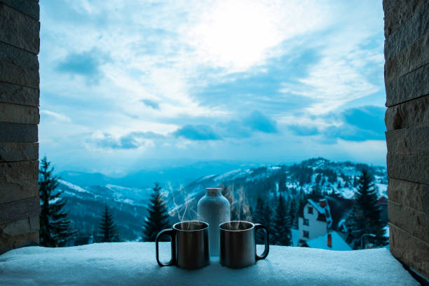 Two metal cups and thermostat bottle in snow at stone window frame on blue hour in mountain landscape background. Copy space