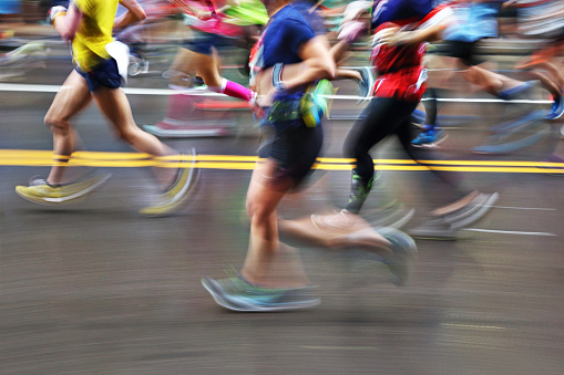 The blurred motion of a group of marathon runners as they run on an urban street. Everyone is unrecognizable by the blur of the motion.