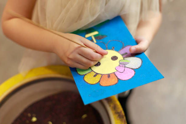 Close-up kid enjoying craft work, sand art painting on sticker card. stock photo