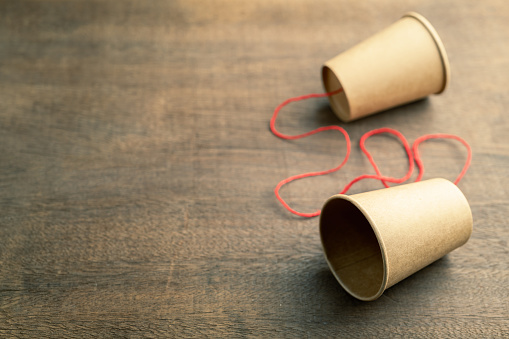 Old style cup phone, two brown paper cups with red string, on wood background, two way communication