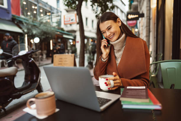 istock Smiling young woman using laptop and and talking on the phone while sitting in cafe 1466386947