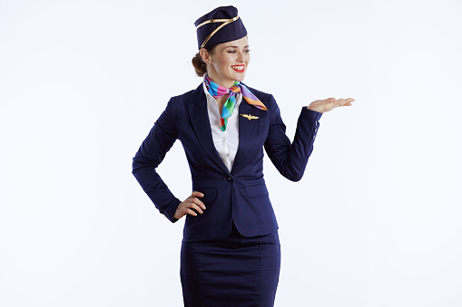 happy stylish air hostess woman against white background in uniform presenting something on empty palm.