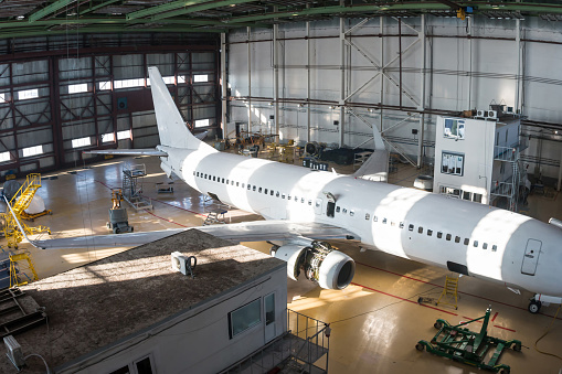 Top view of a white passenger aircraft in the hangar. Airplane under maintenance. Checking mechanical systems for flight operations