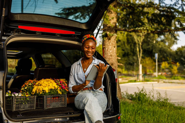 istock Young woman sitting in open car trunk, using digital tablet 1466389797