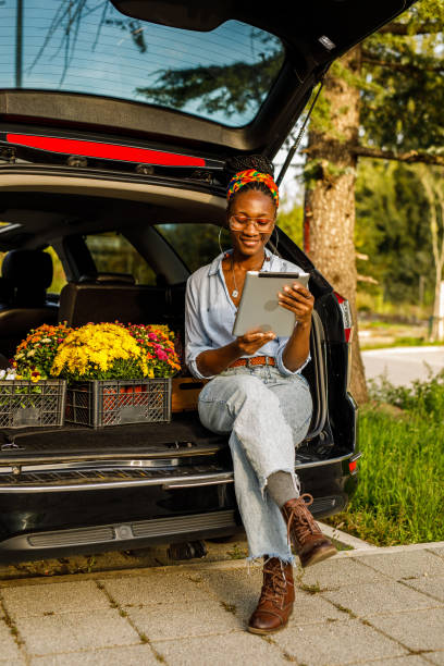 istock Young woman sitting in open car trunk, using digital tablet 1466389799