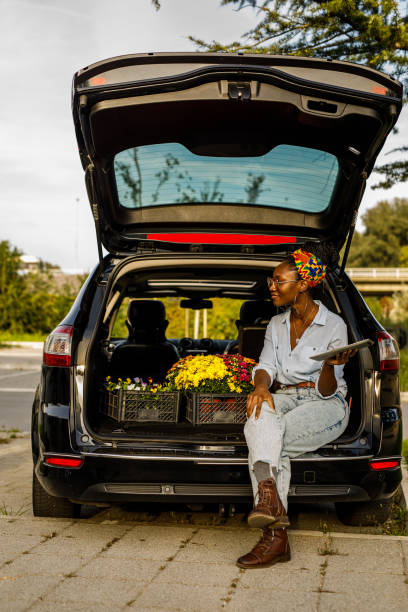 istock Young woman sitting in open car trunk, using digital tablet 1466389802