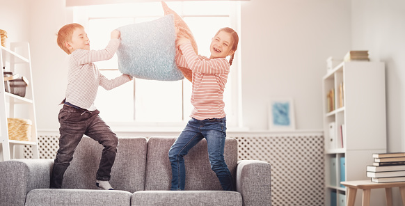 Cute children fighting by pillows on the sofa. Concept of friendship and relationship in the family.