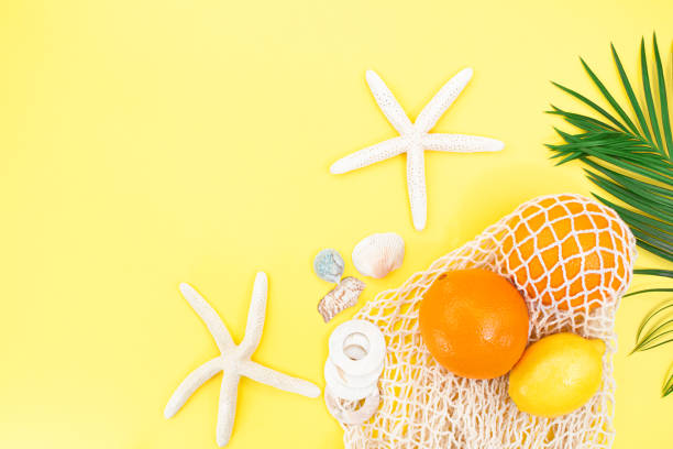 istock Starfish, shells with bag string bag with oranges and lemon with palm branch from the side on yellow background. Concept of summer time, vacation, travel. Copy space 1466403070