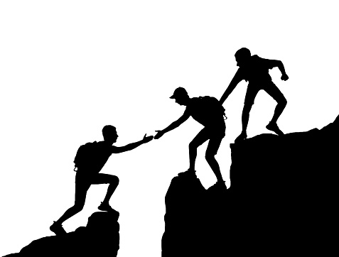 The silhouette of two climbers in the mountains helps another climber overcome an obstacle. Business concept of teamwork and mutual assistance