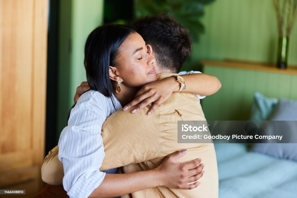 Loving woman hugging her upset husband in their bedroom at home Young woman consoling her husband with a hug while sitting together on their bed at home Embracing Stock Photo