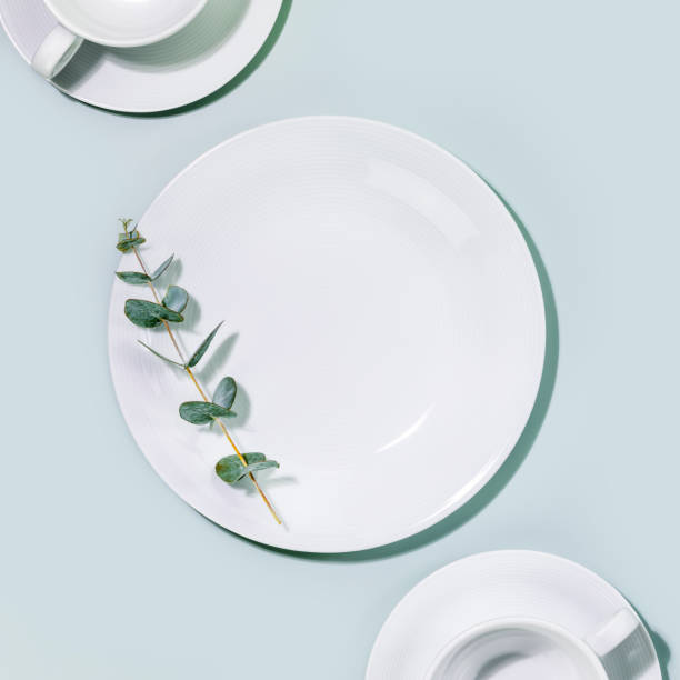 istock Empty white dishes and cups with eucalyptus twig on blue background 1466409854