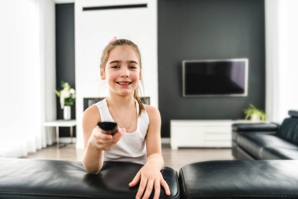 istock Little girl with remote control watching tv on couch 1466410621