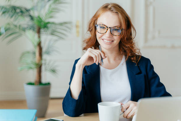 istock Young successful female entrepreneur prepares report for startup project, searches information on laptop computer, concentrated on her task, holds cup of coffee, pen keeps hand under chin poses indoor 1466412092