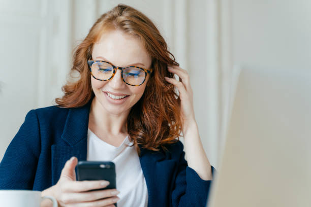 istock Satisfied red haired female uses modern electronic device for checking newsfeed, online communication and searching information, sits in coworking space, uses high speed internet connection. 1466412095