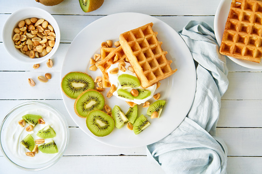 Waffles, kiwi and peanuts with curd cheese on a wooden table