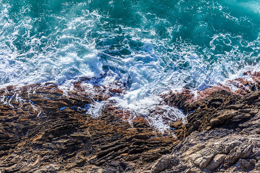 Waves crash and splash on rocks, aerial view from the top