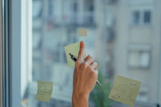 istock Woman writing ideas on sticky notes on glass in home office 1466423650