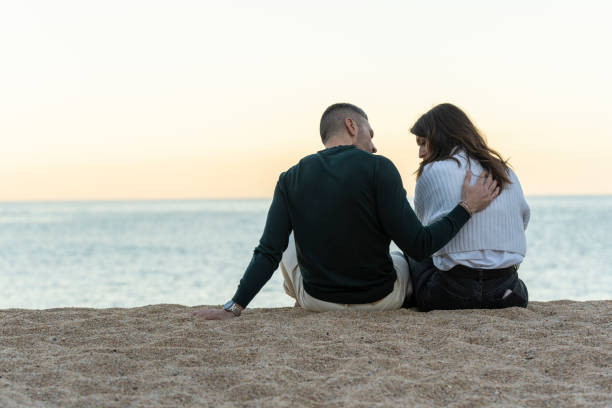 mężczyzna pocieszający jej przyjaciela, siedząc na piasku na plaży - embracing heterosexual couple men women zdjęcia i obrazy z banku zdjęć