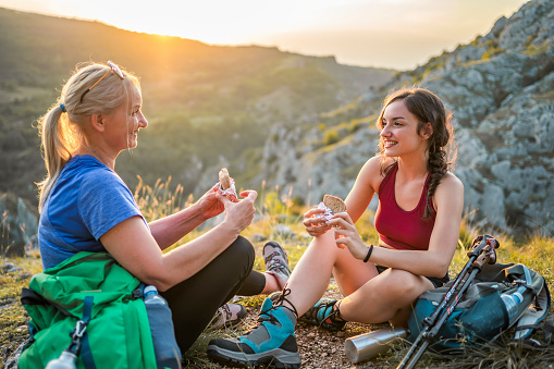 Cheerful mother and daughter taking a break from hiking and eating sandwiches