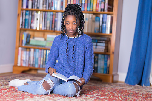 Black girl of 12 reading at home, sitting on the floor.