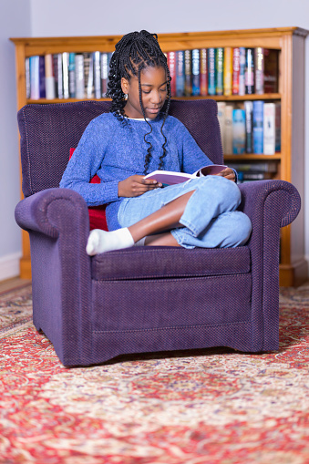 Pretty young black girl sitting in her armchair reading a book.