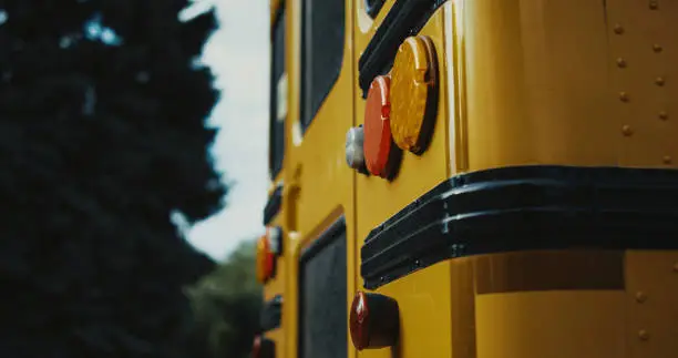 Rear view school bus yellow red headlights parking outdoors close up. Warning stop lights on schoolbus back. Children vehicle transport standing empty road summer day. Safety transportation concept.