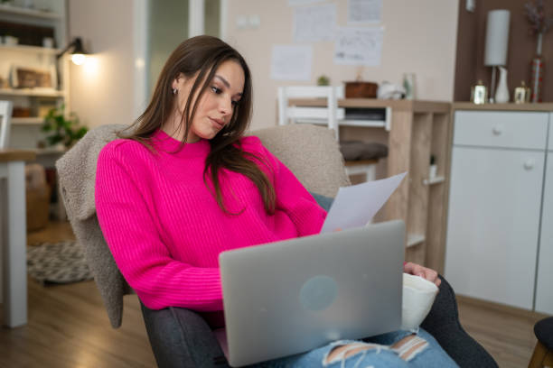 istock One young woman use laptop computer at home hold paper document read 1466434813