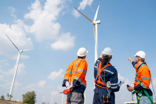 istock Three engineers or technician workers work together in front of cluster of windmill or wind turbine with blue sky and some cloud in their workplace. 1466437252