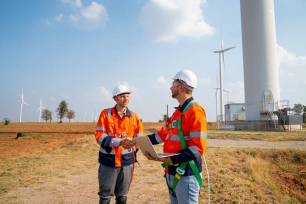 istock Two Caucasian engineers or technicians shake hands and stay in front of cluster of windmill or wind turbine after success the project in workplace. 1466437396